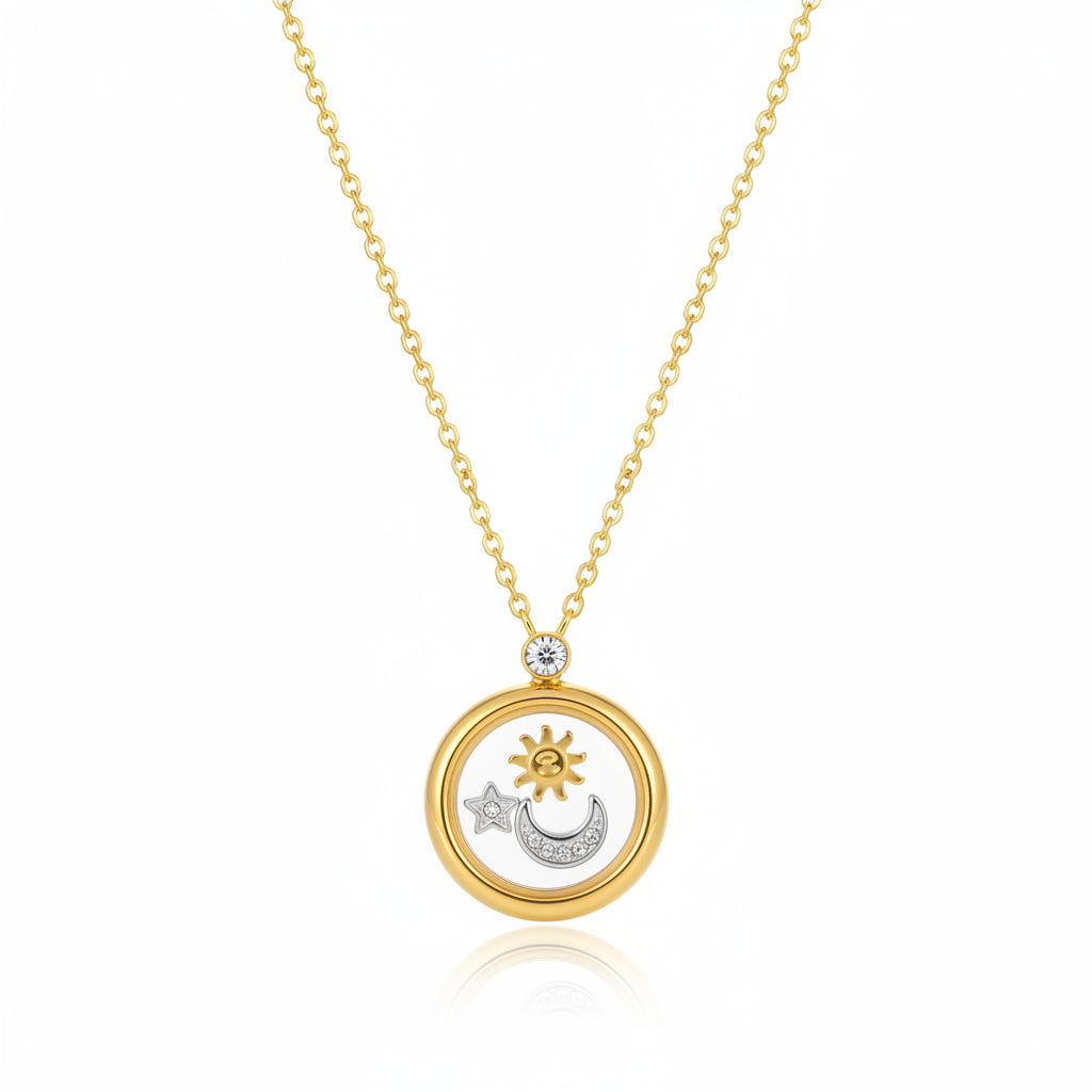 A gold-toned locket necklace with a sun, moon, and star pendant, styled on a textured cream surface next to natural stones.