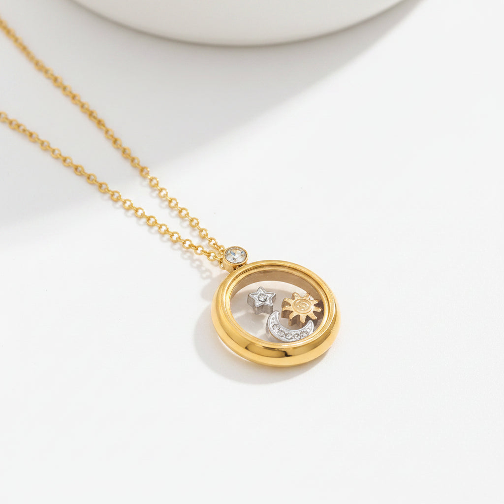 A gold-toned necklace with a circular pendant containing small celestial charms, displayed on a textured beige surface.