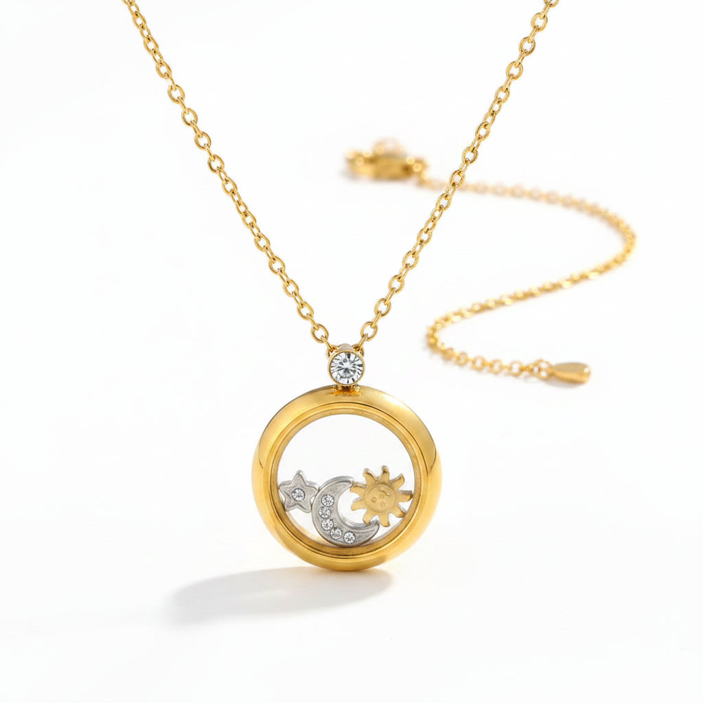 A gold locket necklace with a clear circular pendant displaying gold and silver celestial charms, resting on a white display bust.