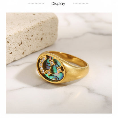 Gold ring with a central gemstone and smaller stones on a textured beige background