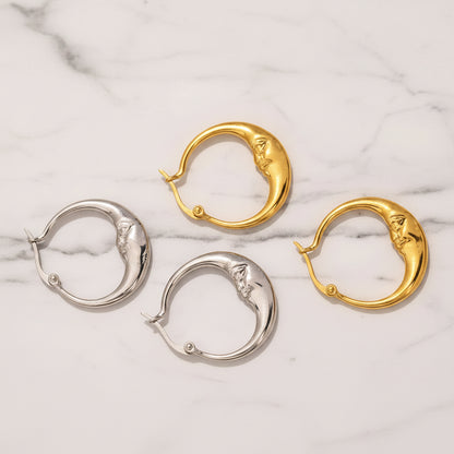 Four dolphin-shaped hoop earrings in gold and silver finishes, displayed on a textured beige surface with a small piece of gold foil in the corner and descriptive text below.
