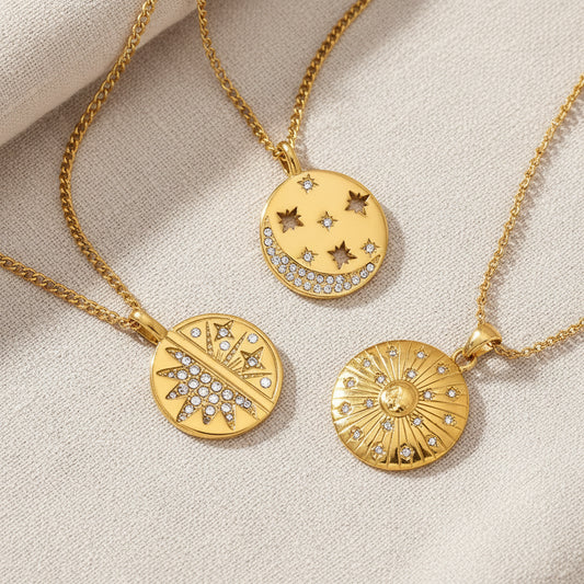 Three gold pendant necklaces with celestial designs are displayed on a white background. The pendants include a crescent moon with stars, a half moon with a sunburst, and a full sunburst with surrounding stars.